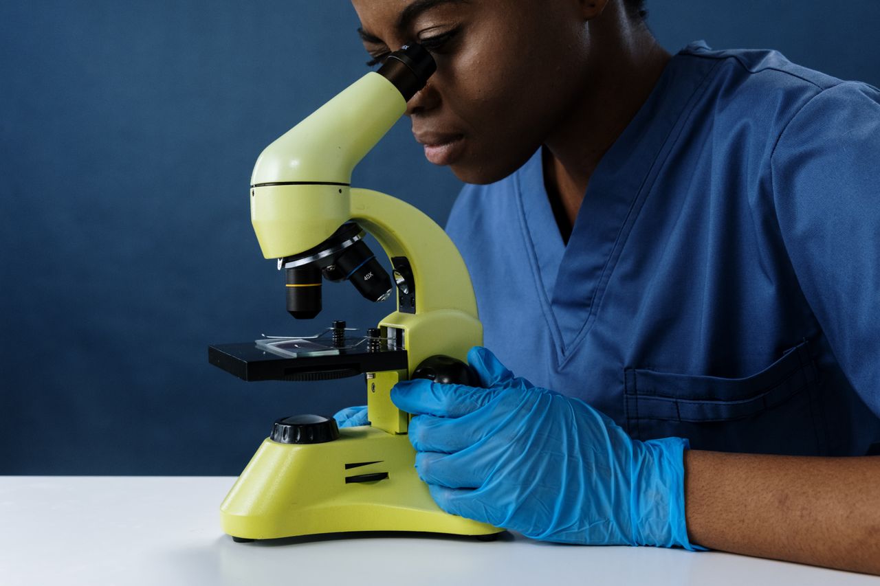 Scientist in scrubs using a microscope in a lab setting.