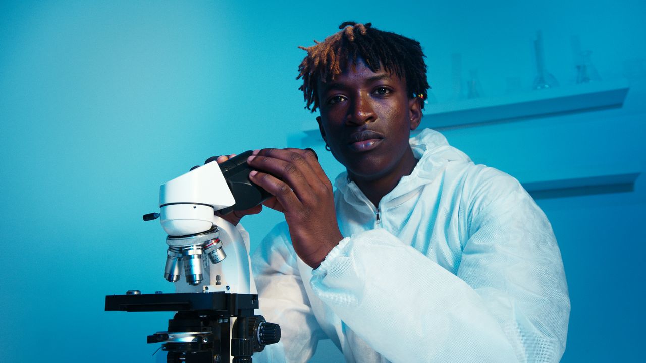 A scientist in protective gear examines a microscope under blue light in the lab.