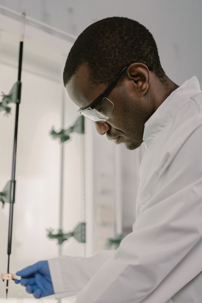 A focused scientist working in a laboratory while wearing protective eyewear and gloves.